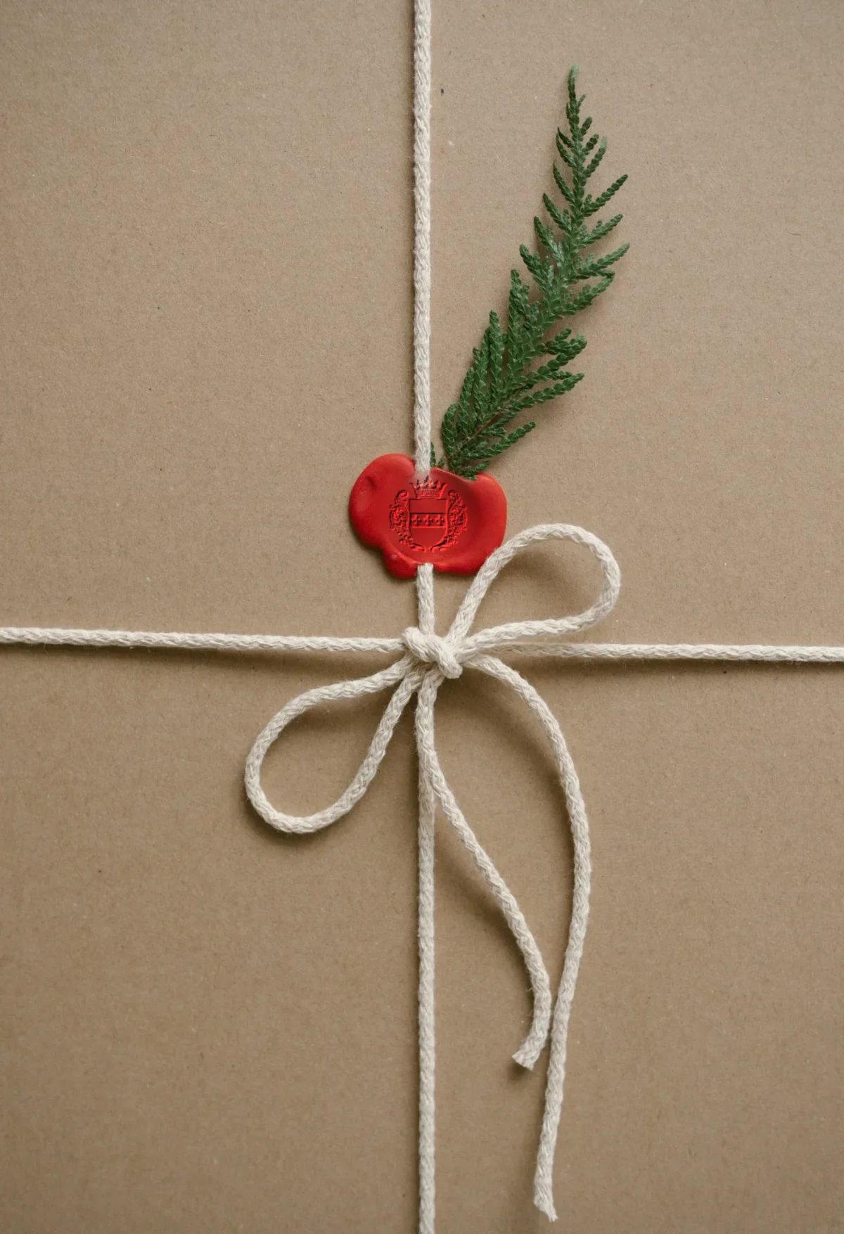 Paquet cadeau en papier kraft, noué d'une ficelle blanche et scellé d'un cachet de cire rouge frappé du blason de la Maison de Pompignac